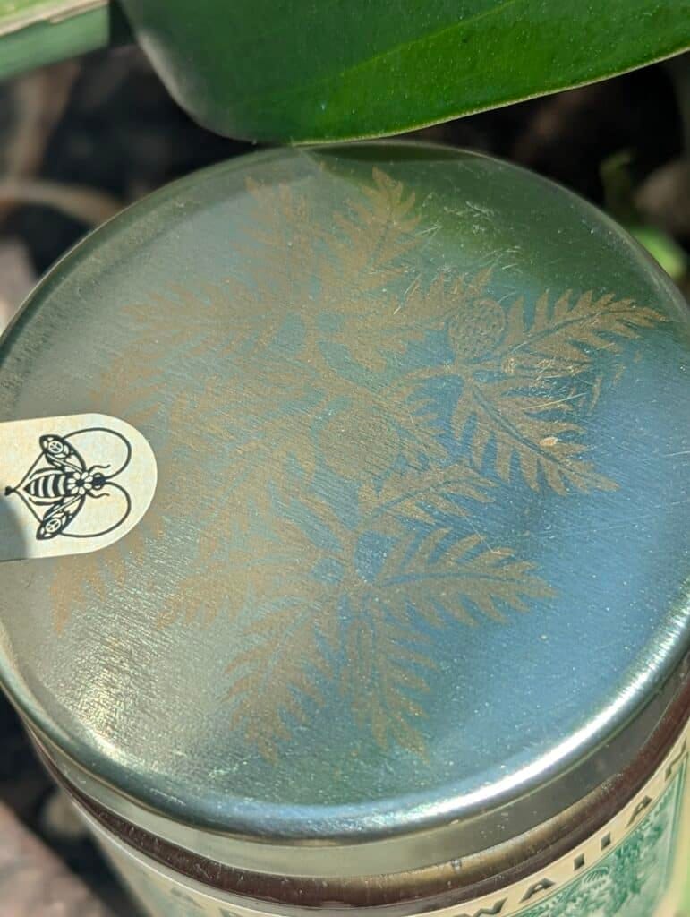 Close-up of honey jar lid with 'Ōhi‘a Lehua design and honey bee logo.