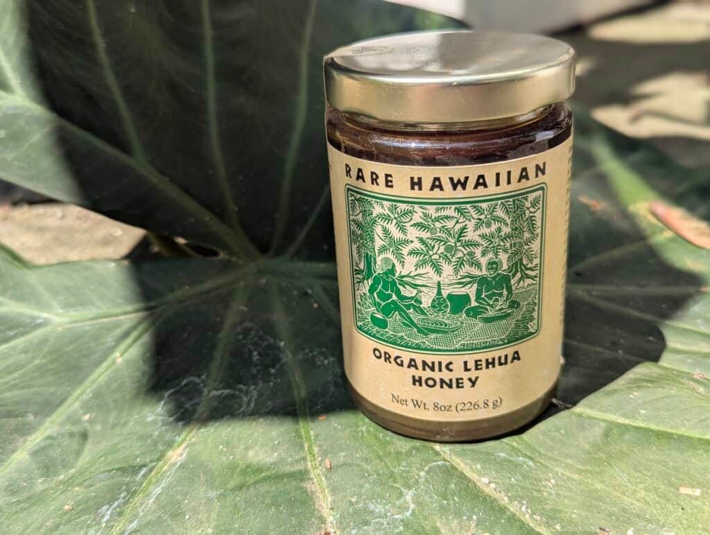 Jar of organic Lehua honey on large green leaves in natural sunlight.